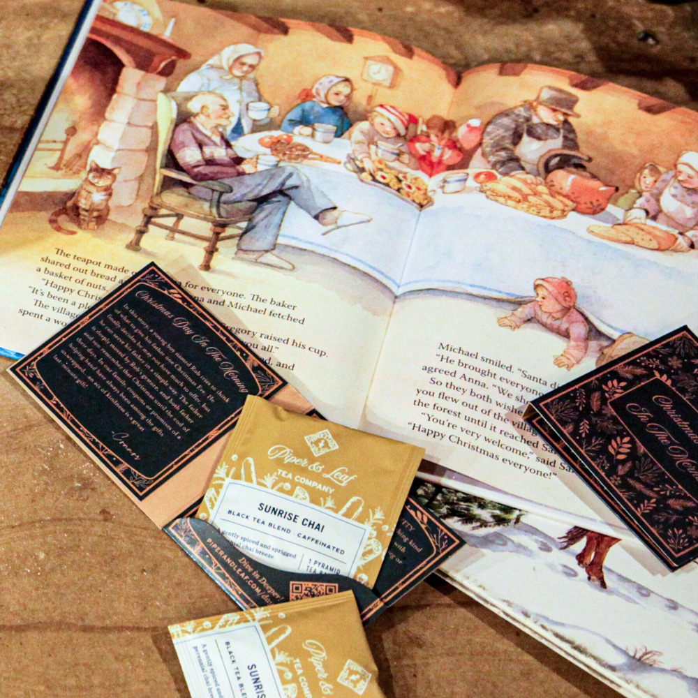 An open illustrated book showcasing a festive scene sits beside three brown and gold tea packets labeled "24 Teas of Advent—Piper and Leaf Advent Calendar 2024" from Piper & Leaf Tea Co., scattered across the table like an Advent calendar of delightful teas.