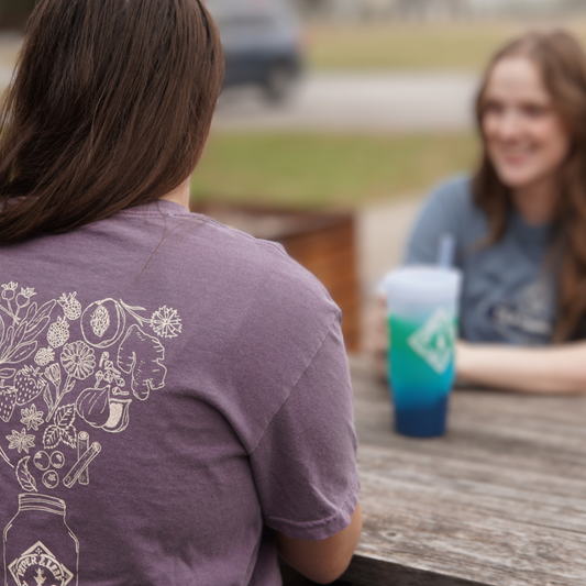 Two women sitting at a table having a conversation while one of them wears a Bouquet of Berries Short Sleeve T-Shirt from Piper & Leaf Tea Co.