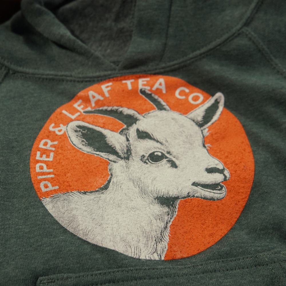An adventurous green Kid's Being Kids-Children's Hoodie with a playful goat from Piper & Leaf Tea Co.