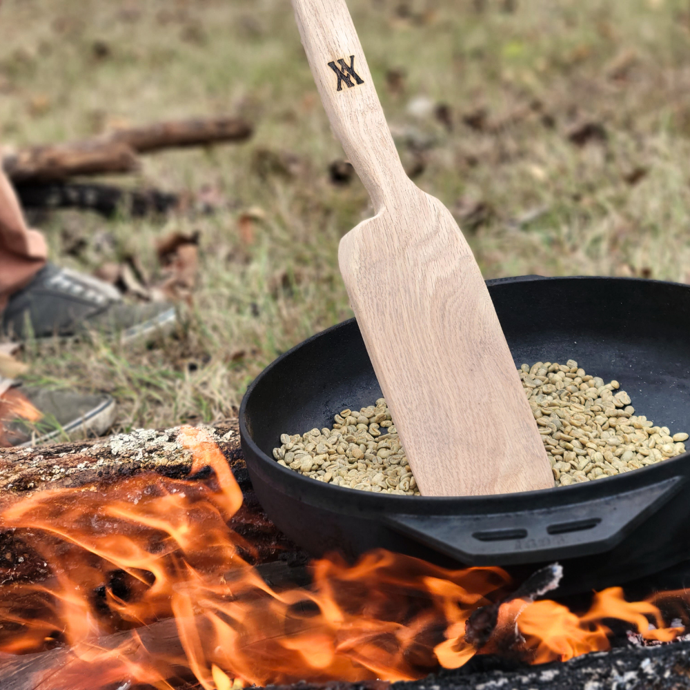 A frying pan with a wooden spatula over a campfire, using traditional roasting methods for Walling Mtn. 12oz Bag of Whole Bean Coffee from Walling Mtn. Coffee.