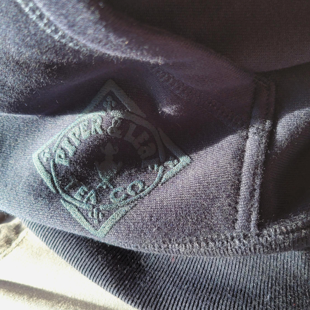 A close up of The Legacy - P&L Collegiate Sweatshirt Hoodie with the Piper & Leaf Tea Co logo on it.