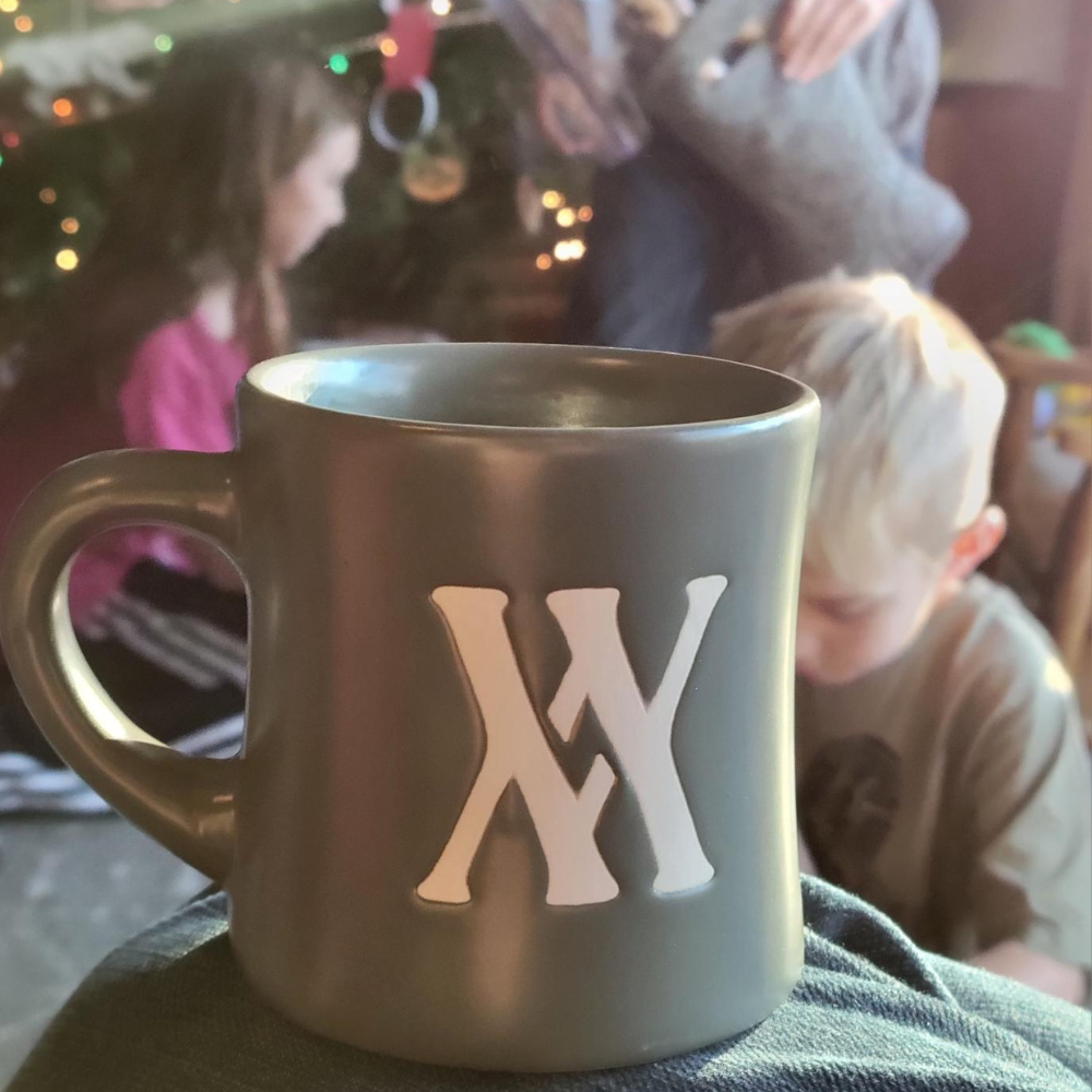 A timeless Piper and Leaf Tea Co. Walling Mountain Farms Mug- 10oz with the letter x on it in front of a Christmas tree.