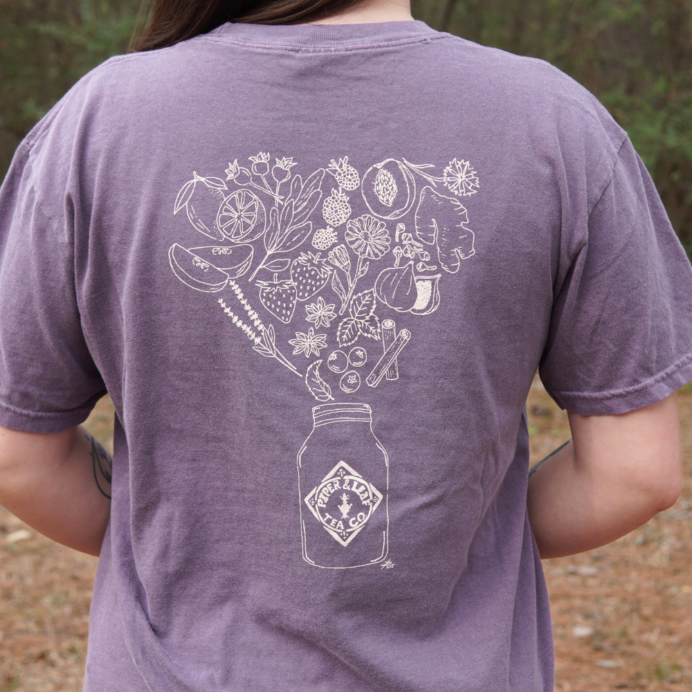 The woman is wearing a purple Bouquet of Berries Short Sleeve T-Shirt featuring a drawing of a mason jar from Piper & Leaf Tea Co.