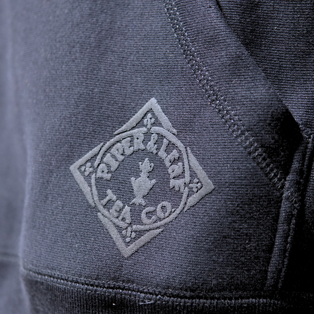 A close up of The Legacy - P&L Collegiate Sweatshirt Hoodie by Piper & Leaf Tea Co with a logo on it.