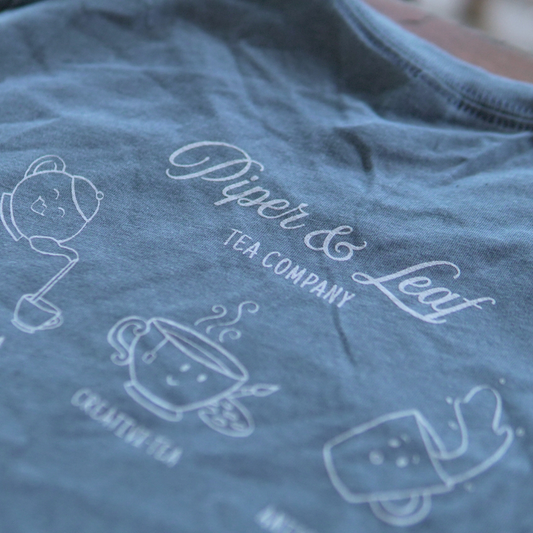 A soft, short sleeve blue t-shirt with screen printed illustrations of Piper & Leaf Tea Co.