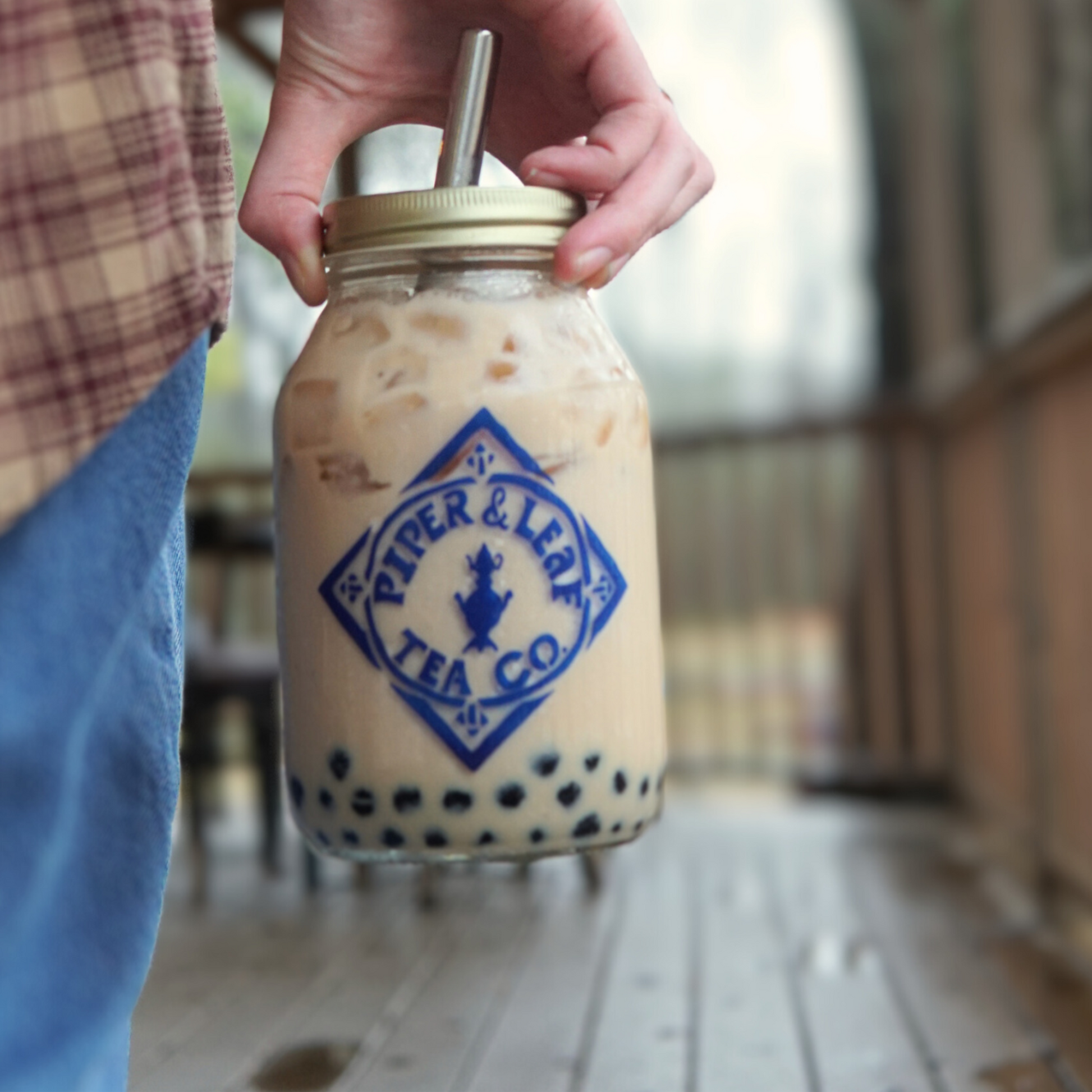 A person holding a Piper & Leaf Tea Co. Boba Tea Lid for Mason Jar with a boba straw.