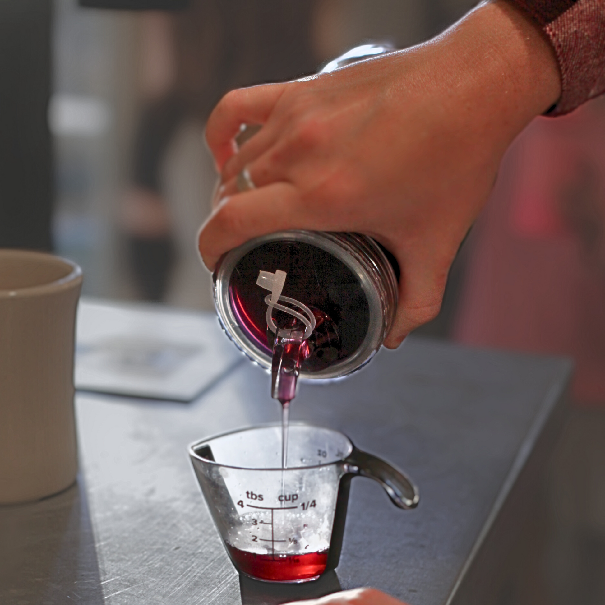 A person pouring Piper & Leaf Tea Co.'s Easy Pour Spout Lid for Mason Jar into a measuring cup.