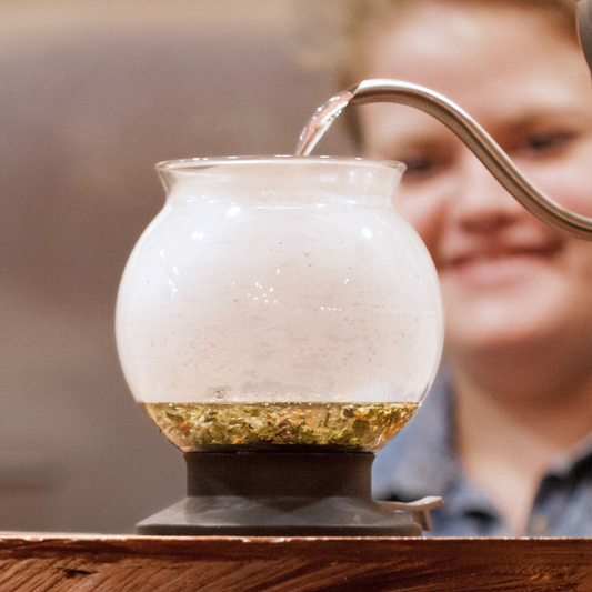 A woman using a Piper & Leaf Tea Co. Hario Largo Glass Tea Infuser Dripper for Loose Leaf Brewing to brew water into a glass bowl.