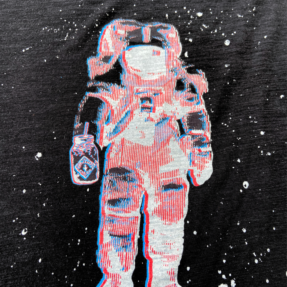 A red and blue graphic print of an astronaut with a retro 3D effect on a black fabric with white speckles can be found on the Limited Edition 3D Vision Space Man Tee by Piper & Leaf Tea Co.