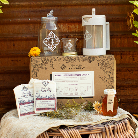 A box of Elderberry Elixir Complete Syrup Kit and other items sits on a wooden table from Piper and Leaf Tea Co.
