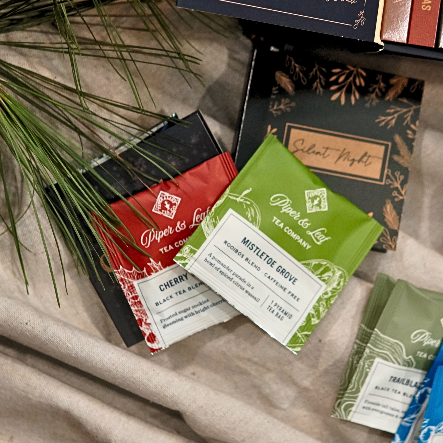 Piper & Leaf Tea Co. Advent Calendar Refill Kit, featuring artisan tea bags like Cherry Christmas, Mistletoe Grove, and Silent Night, displayed on beige fabric with pine needles.