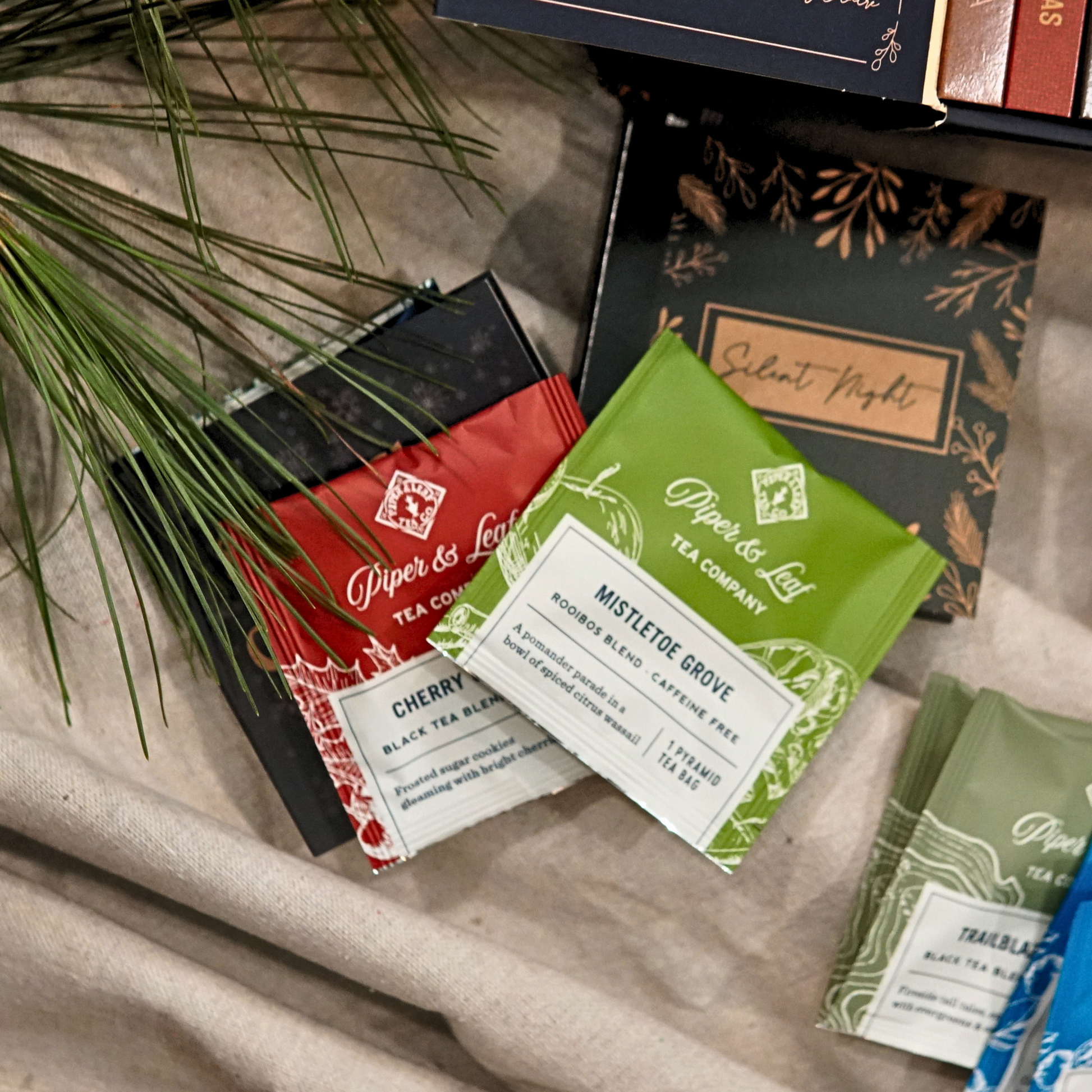 Piper & Leaf Tea Co. Advent Calendar Refill Kit, featuring artisan tea bags like Cherry Christmas, Mistletoe Grove, and Silent Night, displayed on beige fabric with pine needles.