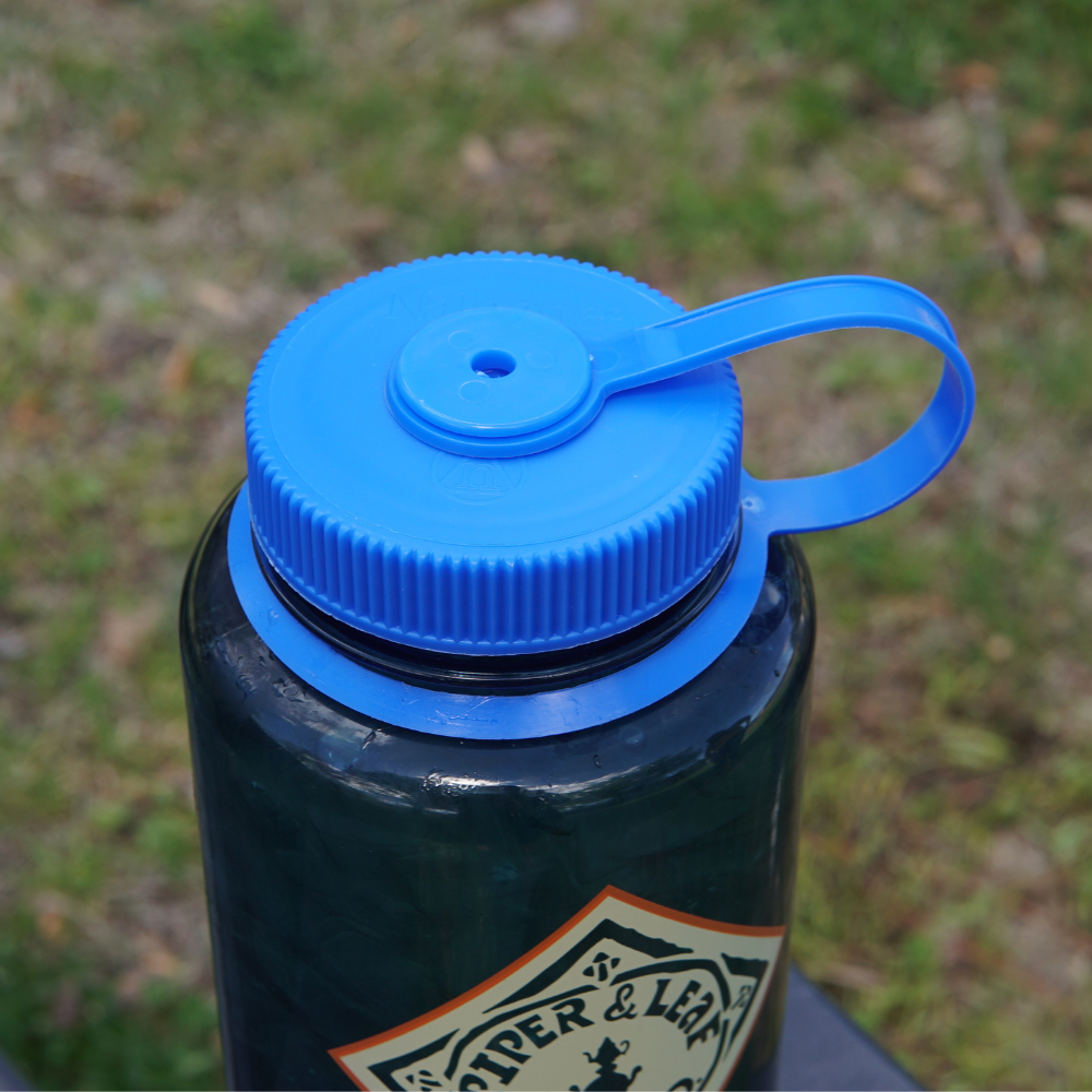 A close-up of a blue, BPA-free Piper & Leaf Nalgene Water (Tea) Bottle- Retro Classic cap with a flip-top lid and carrying loop.