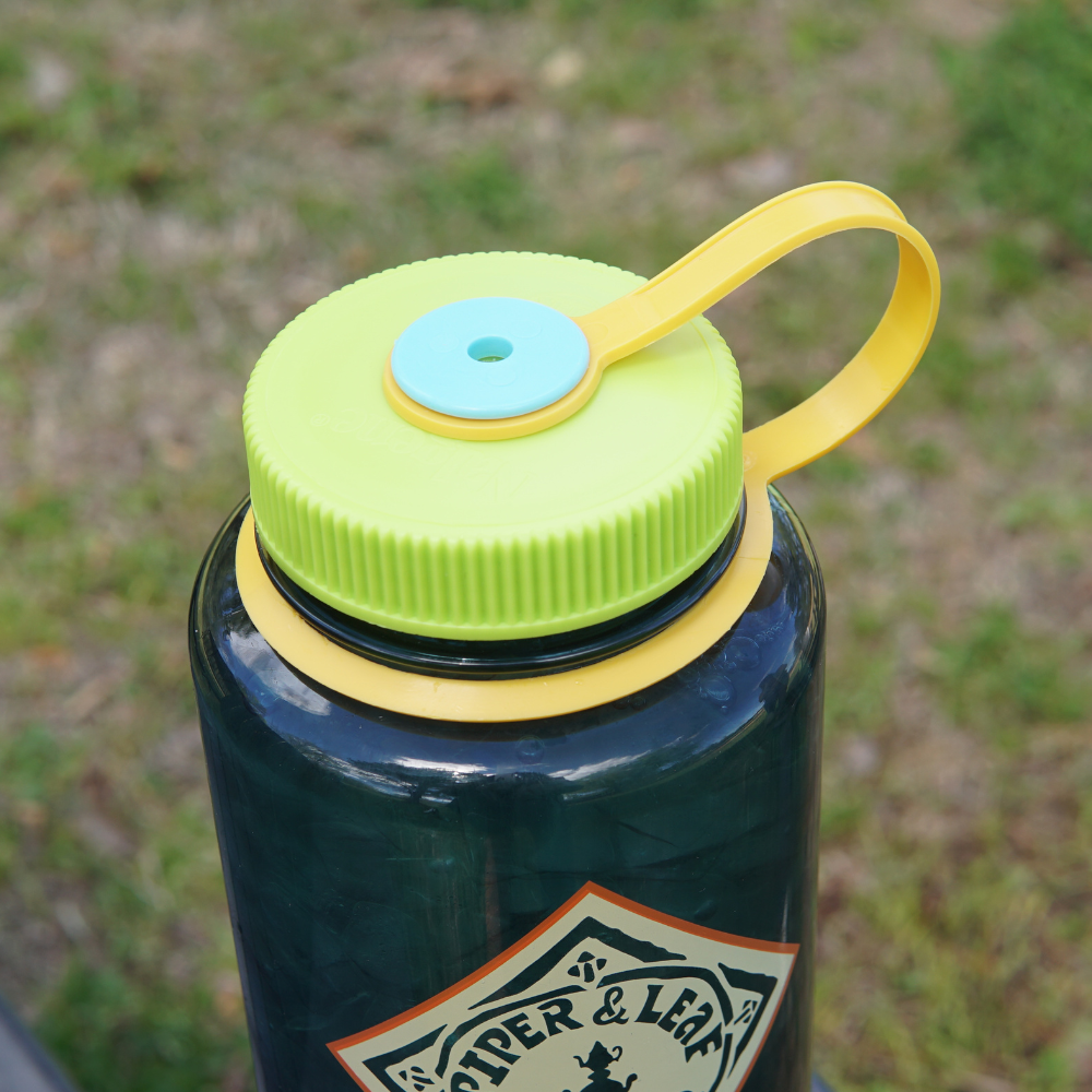 A close-up of a BPA-free Piper & Leaf Nalgene water bottle with a colorful lid and carrying handle.
