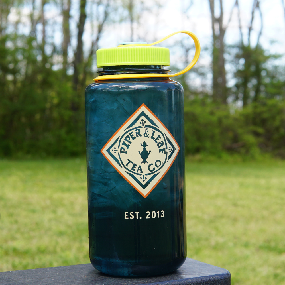 A blue colored glass jar with the logo of "Piper & Leaf Tea Co." outdoors on a sunny day, now featuring Piper & Leaf Nalgene Water (Tea) Bottle- Retro Classic splash cover inserts.