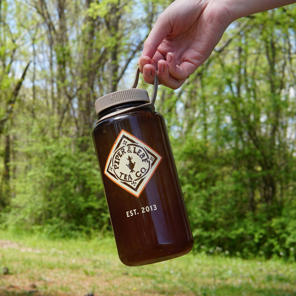 A hand holding a BPA-free Piper & Leaf Nalgene Water (Tea) Bottle- Retro Classic filled with iced tea outdoors.