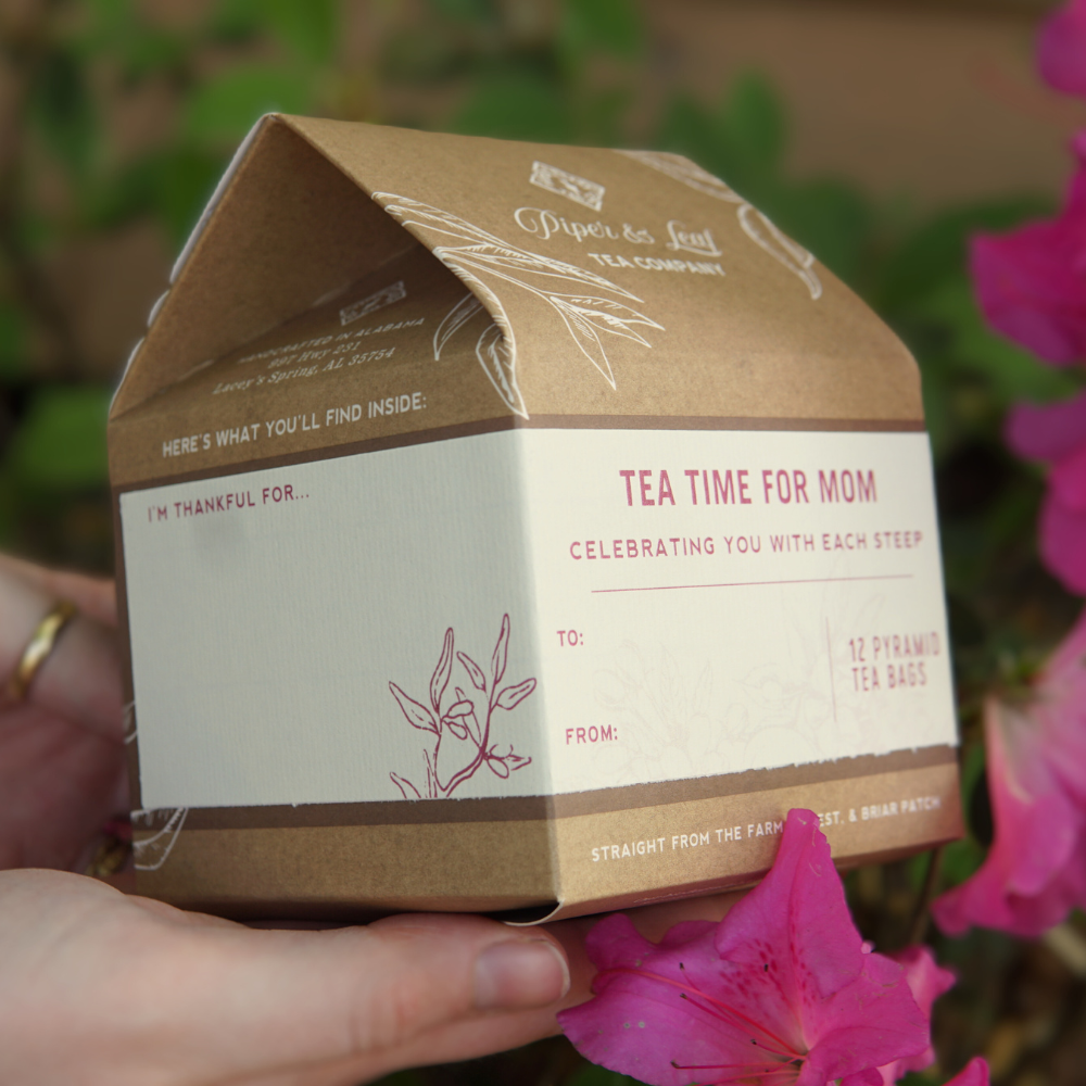 A person holding a Piper & Leaf Tea Co. Mother's Day tea gift box labeled "Tea Time For Mom" with a floral design, featuring space to personalize "to" and "from" fields.
