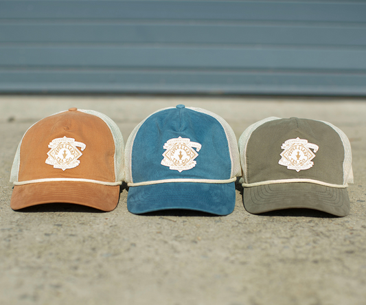 Three P&L Anniversary Soft Trucker Hats with a crest on them, each representing a unique community from Piper & Leaf Tea Co.