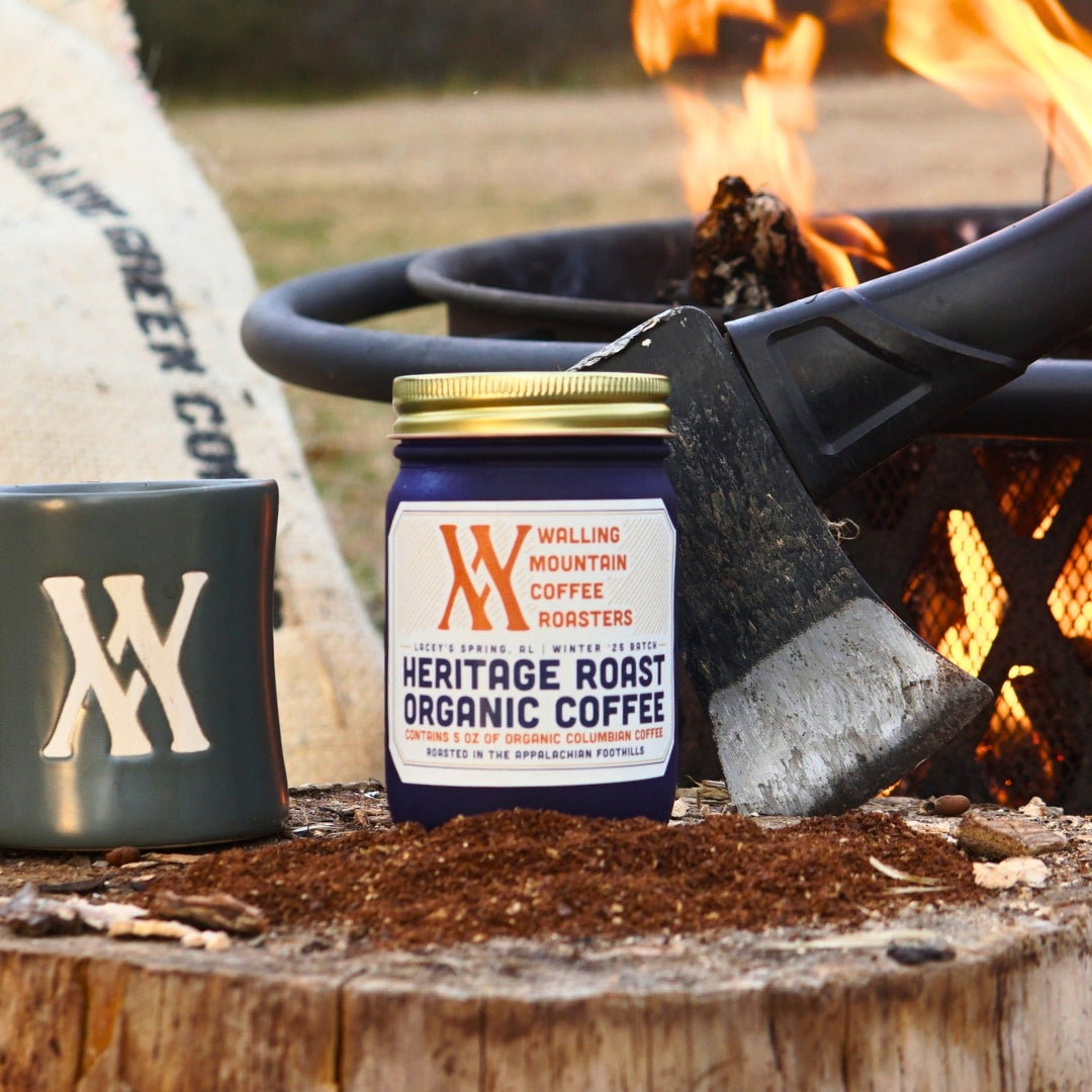 A 5oz jar of Walling Mtn. Coffee's Heritage Roast sits beside a mug and an axe by the cozy fire pit.