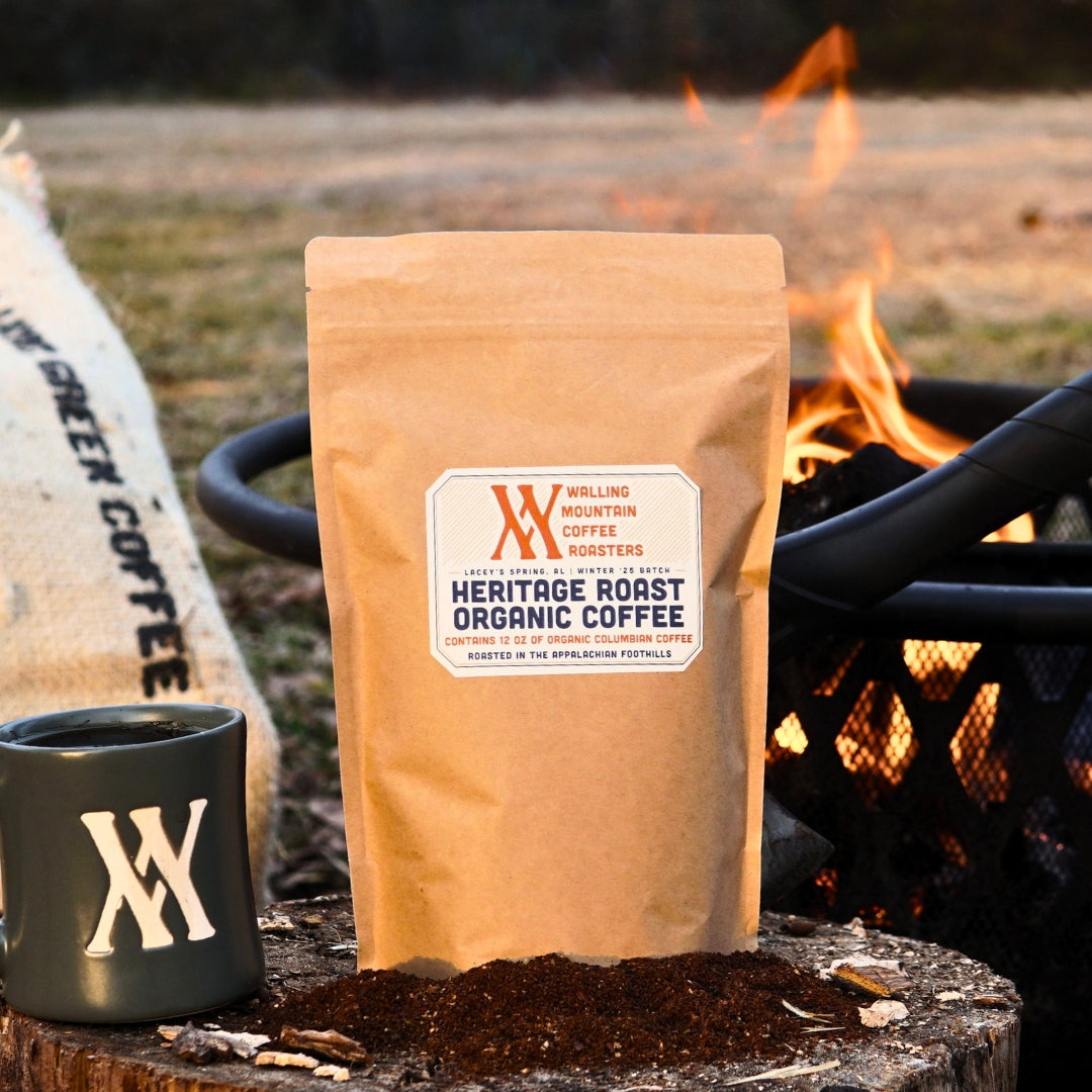 A 12oz bag of Walling Mtn. Heritage Roast Coffee sits by a campfire next to a branded mug, with a coffee sack in the background paying homage to its origins at Walling Mountain Farms.