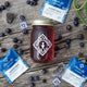 Jar of Blueberry Jubilee next to  single packages on a wooden surface with blueberries.