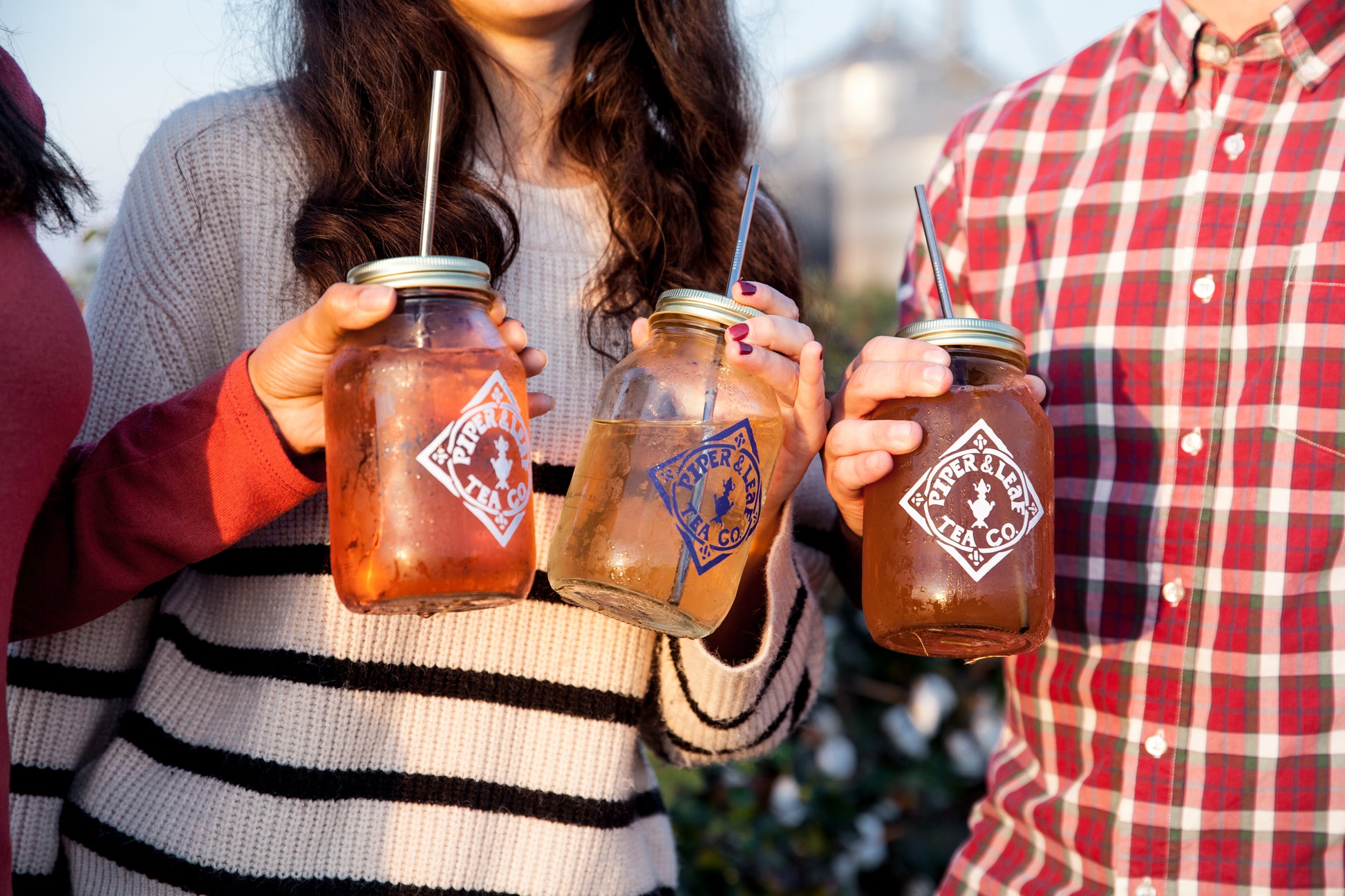 Three sustainable farmers holding Piper & Leaf Tea Co.'s Signature Mason Drinking Jars - Quart Size with drinks in them.