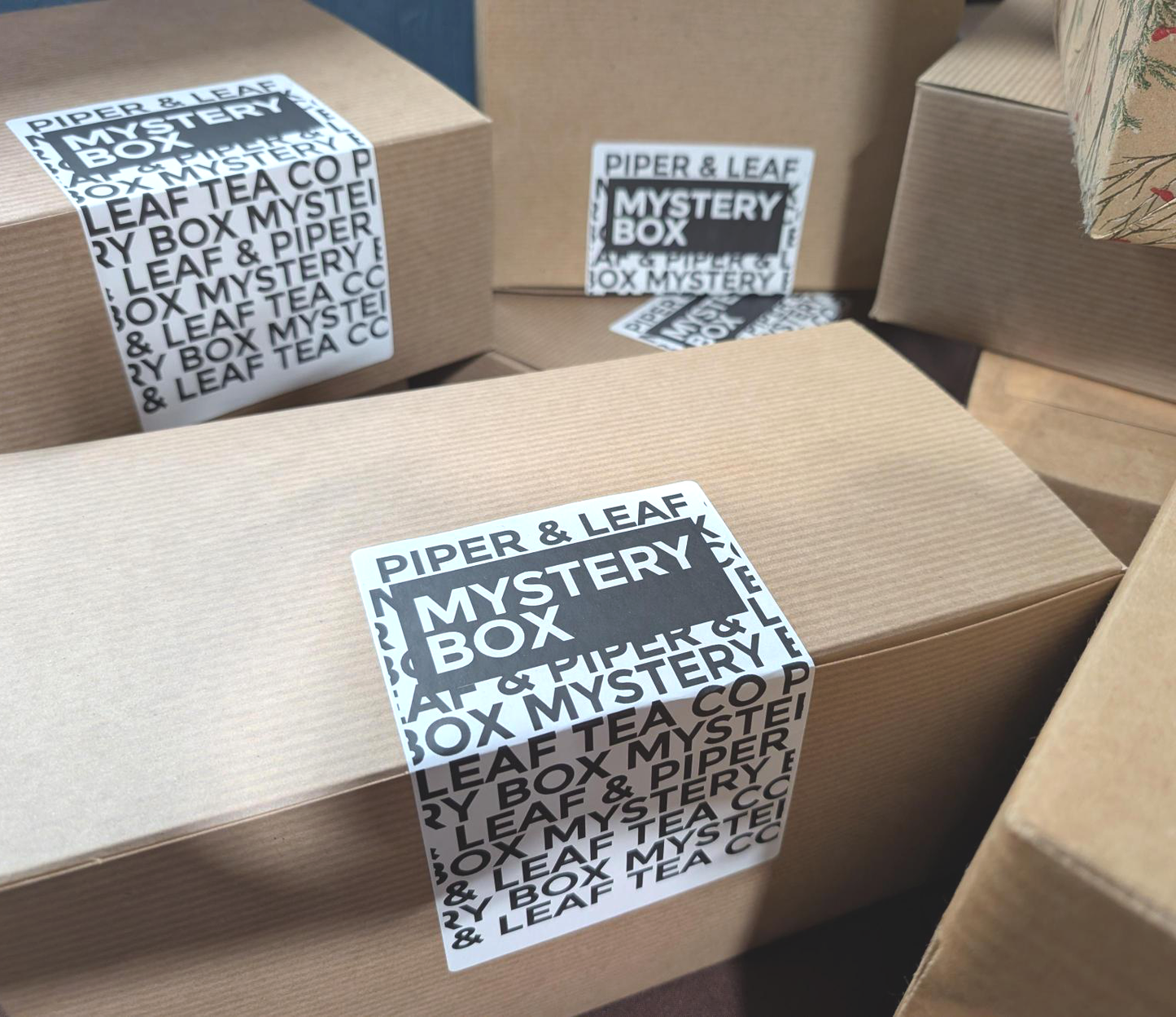 Several brown cardboard boxes labeled "Mystery Box" from Piper and Leaf Tea Co. are stacked together, each with a black and white sticker—making the perfect tea gift for any enthusiast.
