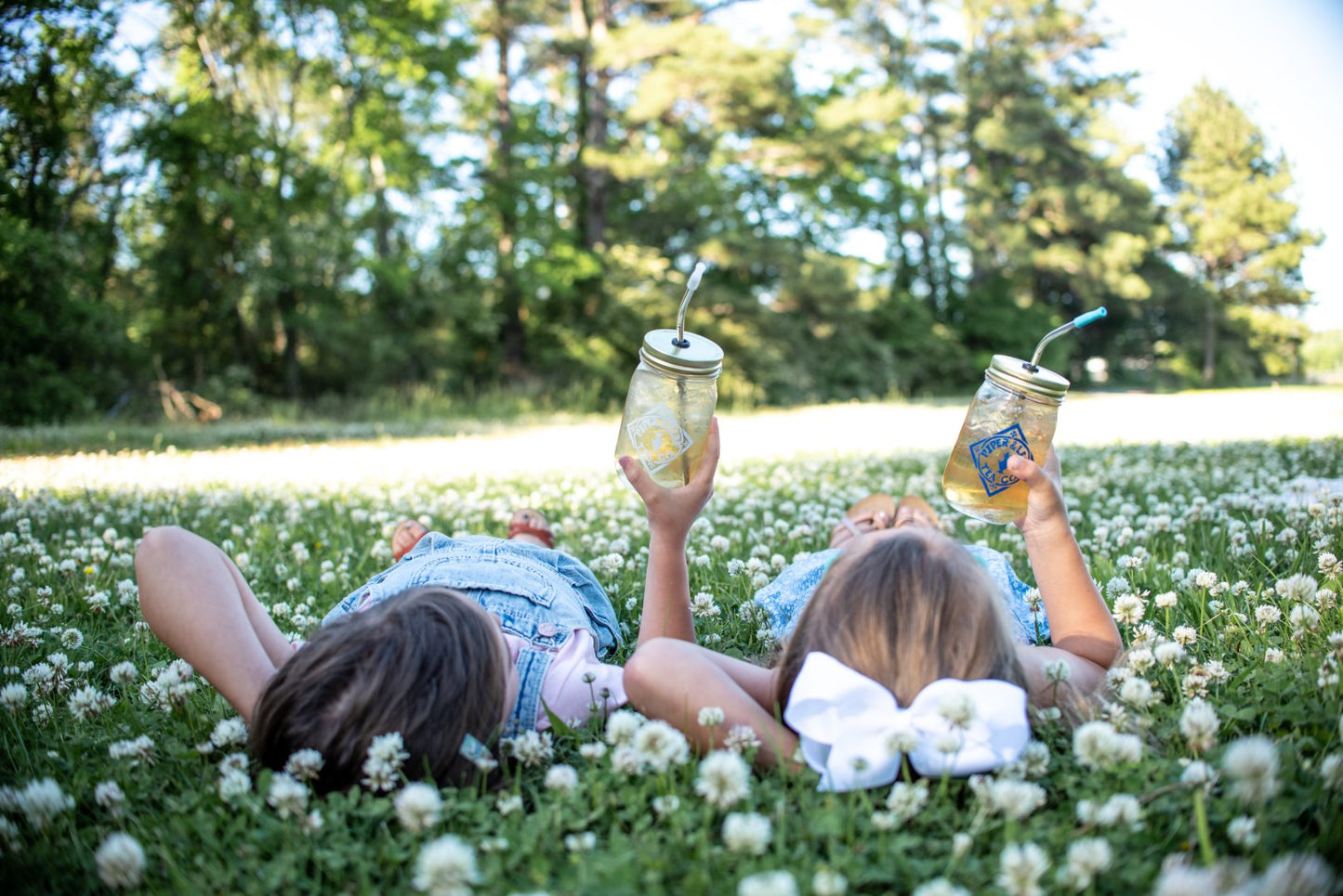 Two sustainable farmers laying in a field with Piper & Leaf Tea Co.'s Signature Mason Jars - Pint Size in their hands.