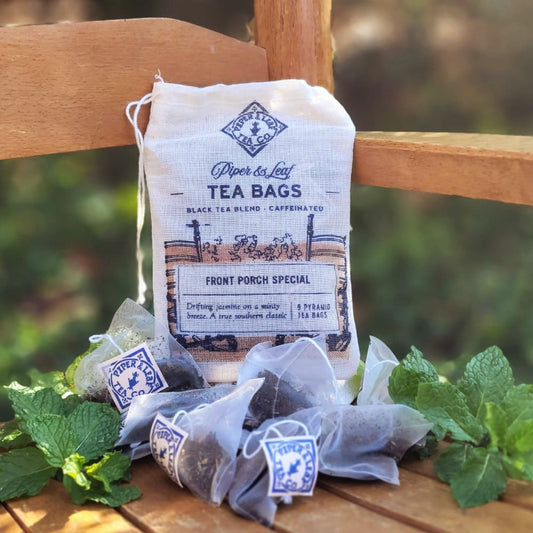 A Front Porch Special 9ct Tea Bag in Muslin, packaged in a pyramid sachet, sitting on a wooden bench.