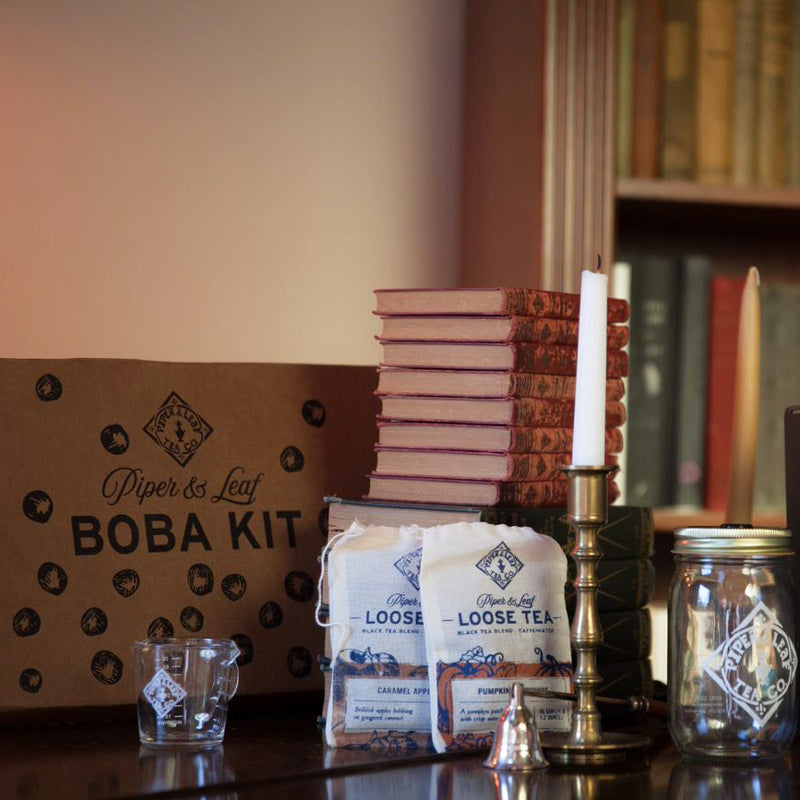 A boba tea kit box next to a stack of books and the fall seasonal blends: Caramel Apple Pie and Pumpkin Moonshine