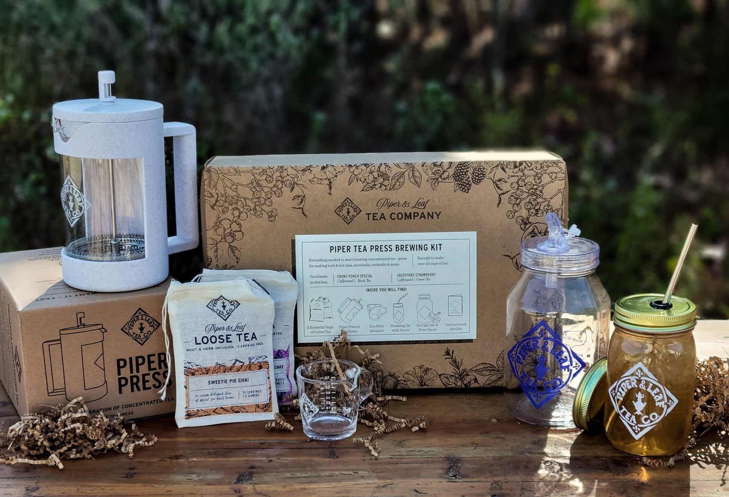 A box with a Piper Press Brew Kit, Piper & Leaf Tea Co. coffee maker, and other items on a wooden table.
