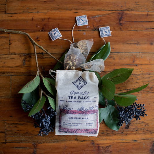 An Elderberry Elixir 9ct Tea Bag in Muslin, possibly infused with elderberries and echinacea, resting calmly on a rustic wooden table.
