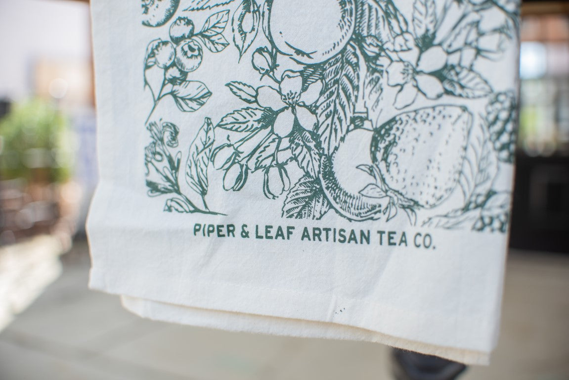 The Garden Tea Party Tea Towel In Garden Green with the Piper & Leaf logo