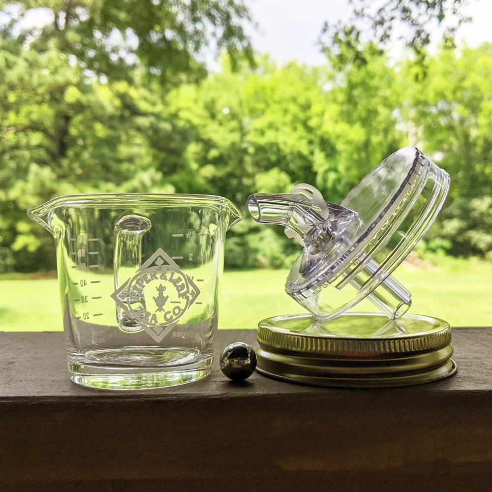 A small measuring cup, a lid with a spout, a solid mason jar lid, and a ball bearing