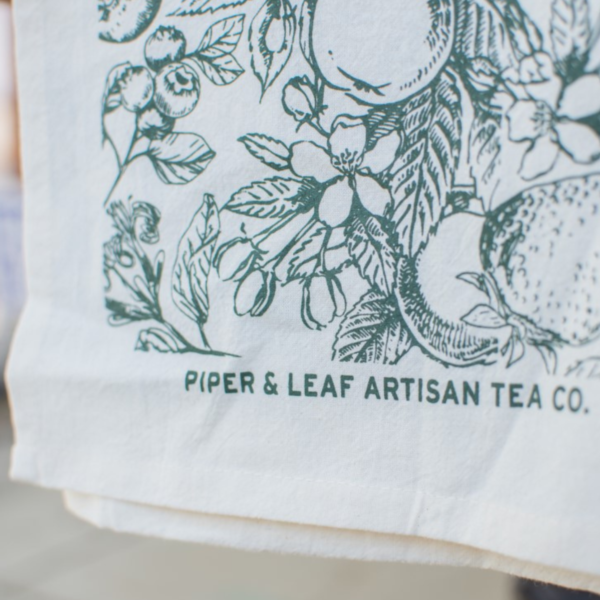 The Garden Tea Party Tea Towel In Garden Green with the Piper & Leaf logo