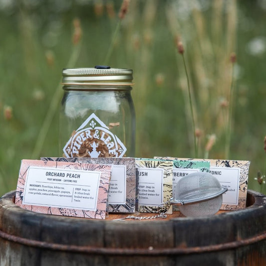 A Teaser Pint Jar Gift Set from Piper & Leaf Tea Co. sitting on top of a wooden barrel.