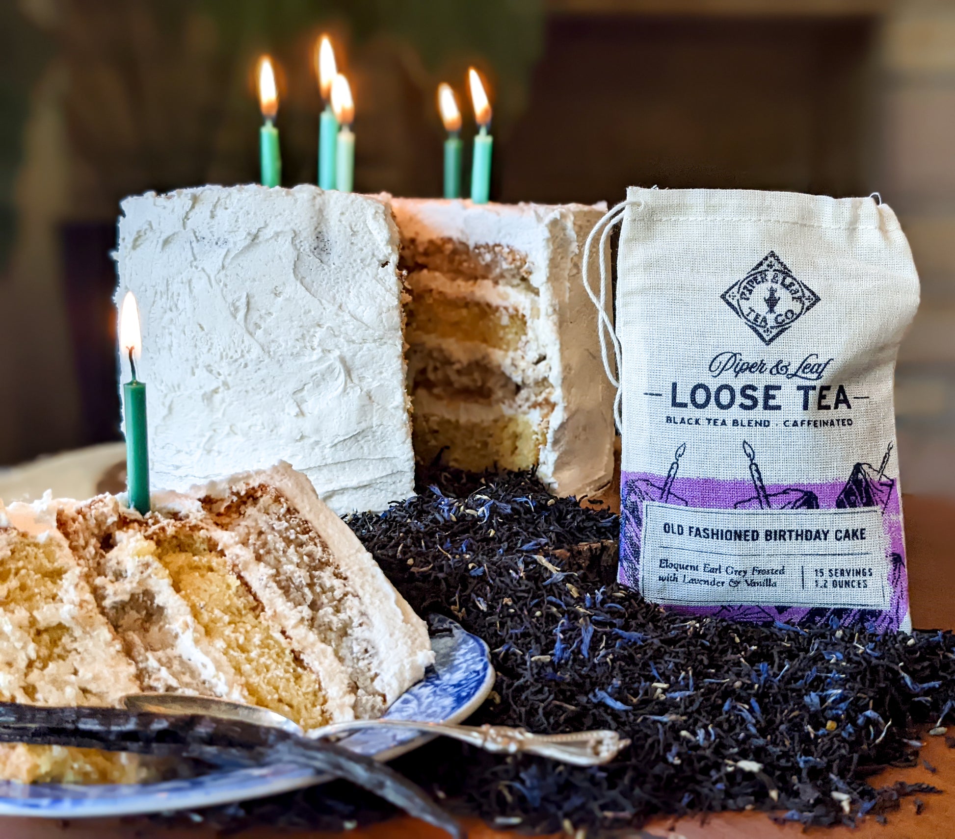 A slice of Piper & Leaf Tea Co.'s Old Fashioned Birthday Cake Muslin Bag of Loose Leaf Tea - 15 Servings with candles and a bag of lavender tea.