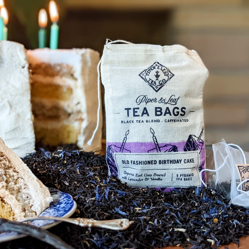 A Old Fashioned Birthday Cake 9ct Tea Bags in Muslin and Earl Grey-infused cake accompanied by lavender-scented tea bags are elegantly arranged on a table. (brand: Piper & Leaf Tea Co.)