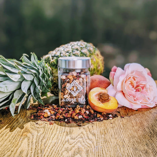 A vibrant jar of Orchard Peach Glass Jar of Loose Leaf Tea - 30 Servings from Piper & Leaf Tea Co. and a tropical pineapple on a wooden table.