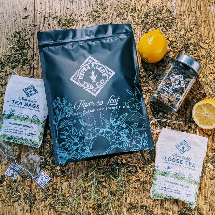 A bag of Springdrop Spritzer Bulk Sachets - 70ct Tea Bags with lemons and herbs on a wooden table by Piper & Leaf Tea Co.