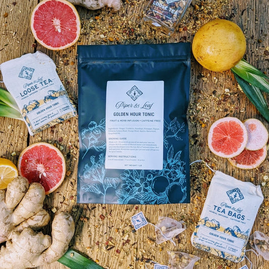 A bag of Golden Hour Tonic Bulk Sachets - 70ct Tea Bags by Piper & Leaf Tea Co. with grapefruits and oranges on a wooden table.