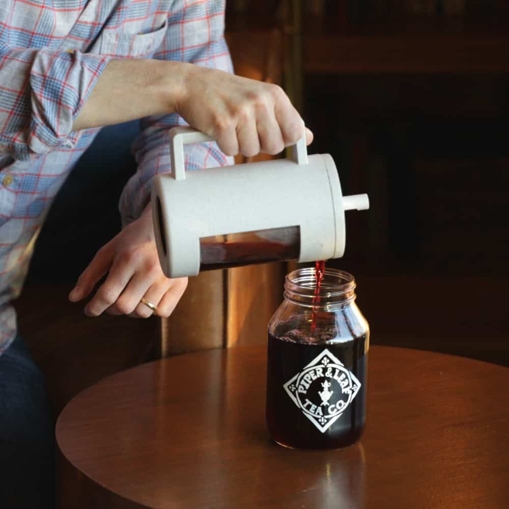Pouring freshly brewed tea out of a Piper Press tea press into a mason jar