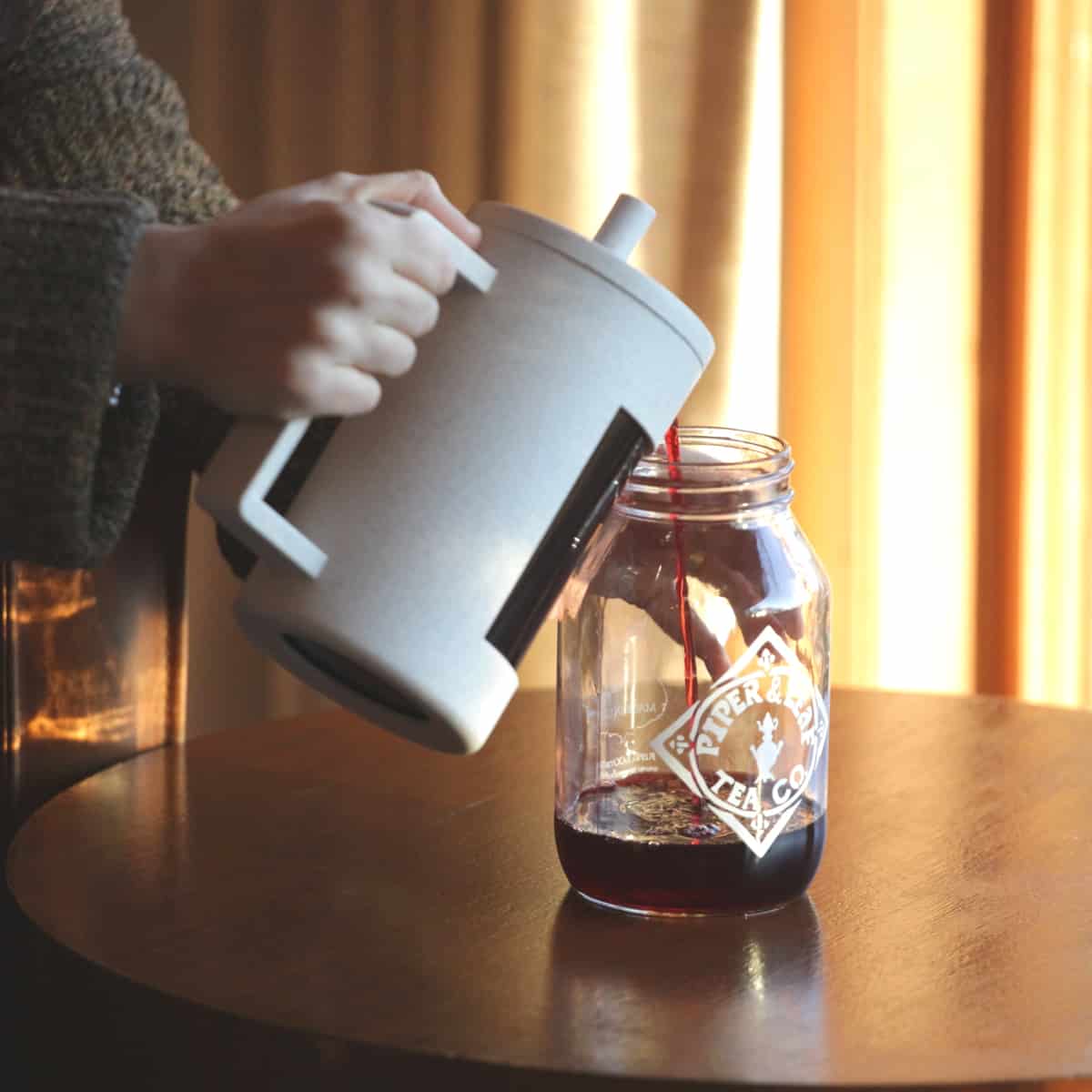 Pouring freshly brewed tea from a tea press into a Piper & Leaf quart jar
