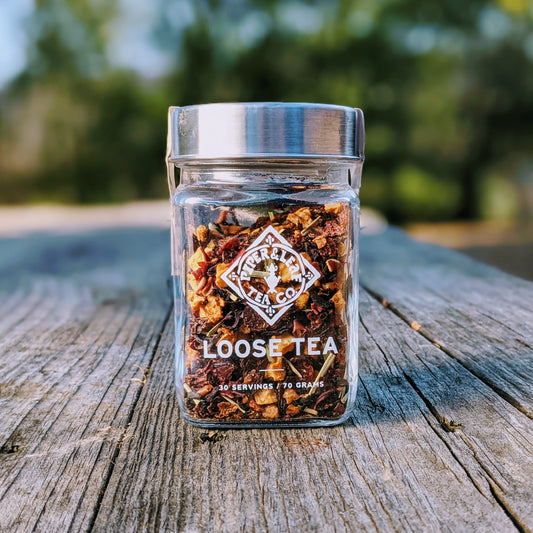 Piper & Leaf Tea Co.'s Strawberry Shindig Glass Jar of Loose Leaf Tea - 30 Servings, caffeine-free, on a wooden table, infused with the flavors of strawberries and lemongrass.