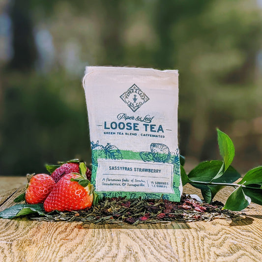 A Sassyfras Strawberry Muslin Bag of Loose Leaf Tea - 15 Servings, from Piper & Leaf Tea Co., sitting on a table next to strawberries and Sencha.