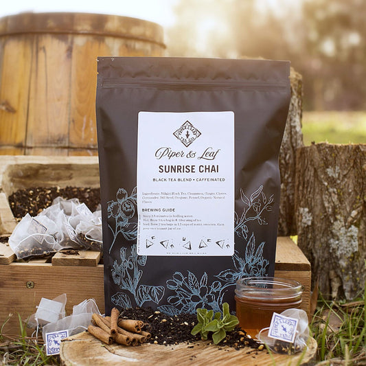 A light bag of Sunrise Chai Bulk Sachets - 70ct Tea Bags from Piper & Leaf Tea Co. sitting on a wooden table next to a wooden barrel.