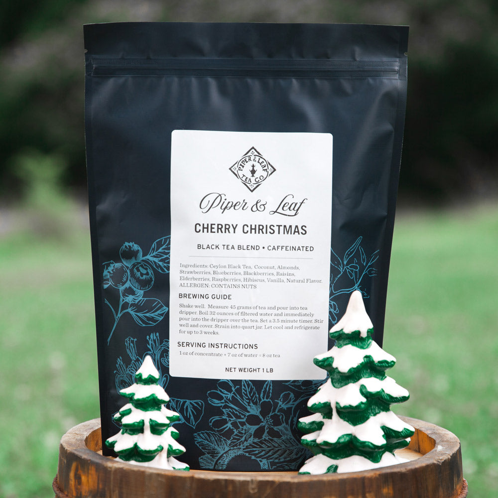 A Cherry Christmas Pound Bag - 190 servings from Piper & Leaf Tea Co. is displayed outdoors, accompanied by two small ceramic pine tree decorations.