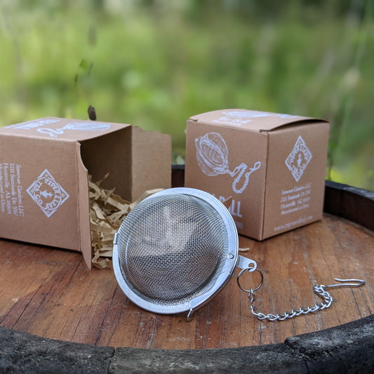 A Piper Tea Ball Extra-Large from Piper and Leaf Tea Co. sits on a wooden table next to a box.