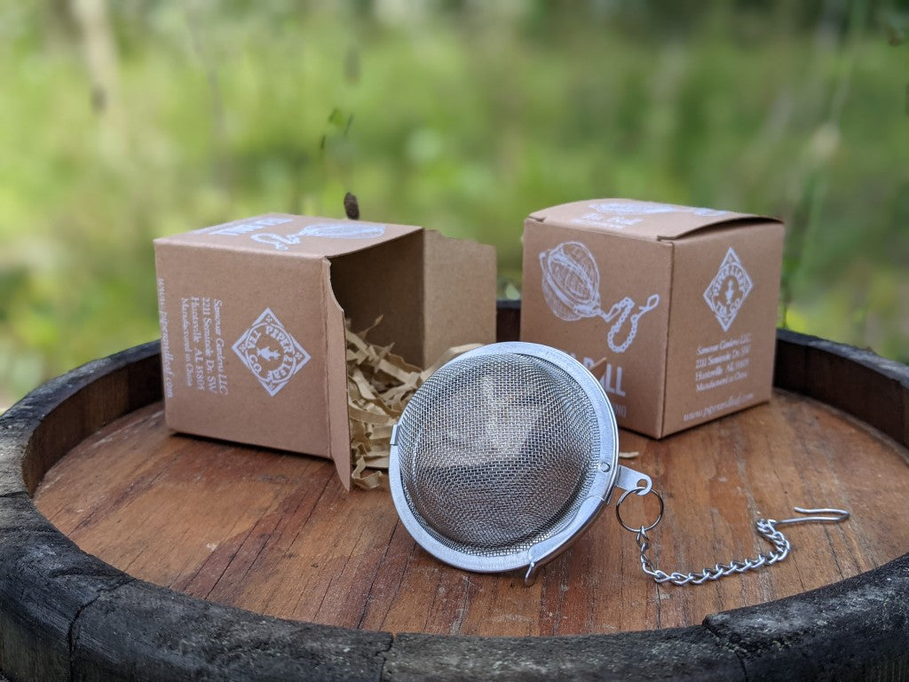 A mesh tea ball in front of two tea ball boxes