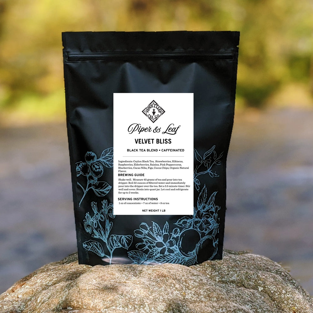 A bag of Velvet Bliss Bulk Sachets - 70ct Tea Bags from Piper & Leaf Tea Co. sitting on a rock next to a river.